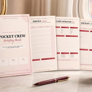May include: A Pocket Crew Briefing Book with a light pink cover featuring black text and three open pages displaying organised flight planning sections. The pages include headers like Service Timeline, Cabin Operator Brief, and Aircraft + Cabin Focus.
