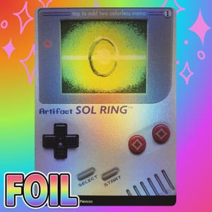May include: A rectangular holographic trading card designed like a handheld game console. The screen displays a Sol Ring graphic with the text tap to add two colorless mana. The card features a directional pad, two red buttons, and select start buttons.