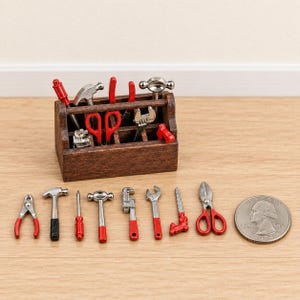Peut inclure: Une boîte à outils miniature en bois contenant divers petits outils en métal avec des accents rouges et noirs, notamment des marteaux, des pinces, des clés et une scie. Une pièce de monnaie est placée à côté pour montrer l'échelle réduite.