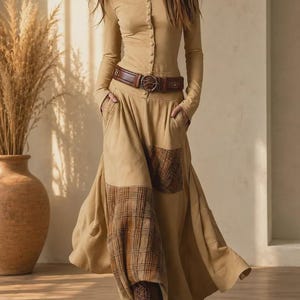 May include: A long-sleeved tan button-down top paired with a matching tan maxi skirt featuring a brown plaid patch pocket and hem detail. The outfit is cinched at the waist with a wide brown leather belt featuring a circular buckle and includes brown lace-up boots.