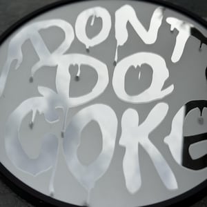 May include: A circular wall mirror with a black frame featuring the text DONT DO COKE in a white, dripping, graffiti-style font across the reflective surface. The lettering appears to be applied to the glass, creating a layered visual effect.