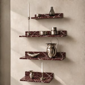 May include: Four wall-mounted floating shelves featuring a deep red marble pattern with white veining. The shelves hold various metallic and glass decorative objects, including a tall candle holder, a silver pitcher, and several small bowls.