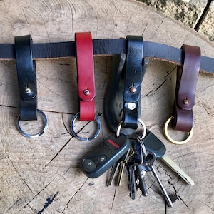 May include: Four leather keyrings with metal rings and a set of keys attached to one of them. The keyrings are in black, red, and brown.