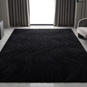 May include: A rectangular black area rug featuring a raised, carved wave pattern across its surface. The rug has a deep, solid black color with flowing, textured lines that create a sense of movement and depth throughout the entire piece.