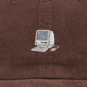 May include: A dark brown corduroy baseball cap featuring a small, detailed embroidery of a vintage beige computer monitor, keyboard, and mouse centered on the front panel. The fabric has a distinct vertical ribbed texture throughout.