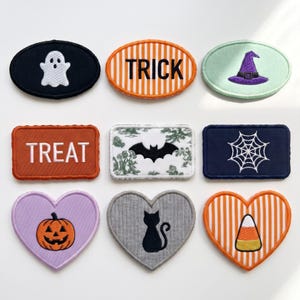 May include: A collection of nine embroidered patches featuring Halloween themes including a white ghost, orange and white stripes with the text TRICK, a purple witch hat, orange with the text TREAT, a black bat, a white spiderweb, a pumpkin, a cat, and candy corn.