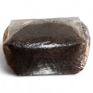 Puede incluir: Un bloque rectangular de sustrato orgánico granular de color marrón oscuro, fuertemente comprimido y sellado dentro de una bolsa de plástico transparente y flexible. El contenido parece ser una mezcla densa y uniforme de tierra o turba.