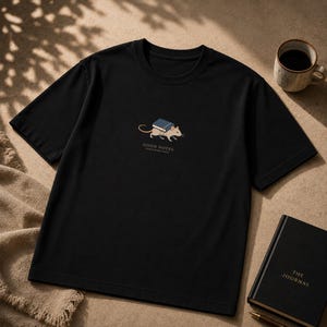 May include: A black short-sleeved t-shirt featuring a graphic of a light brown mouse carrying a blue book on its back. Below the mouse, the text reads GOOD NOTES and below that, in smaller letters, STUDY HARD DAYS. The shirt has a crew neckline.