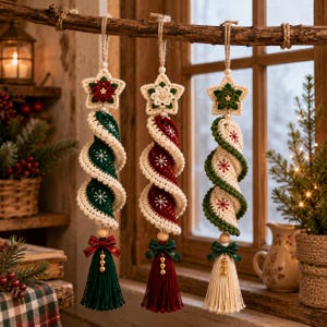 May include: Three hanging spiral ornaments made of crocheted yarn. Each features a star at the top, a twisted body with snowflake embroidery, and a bottom tassel with a small bow and beads. The colors are dark green, deep red, and cream white.
