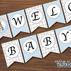 Può includere: Uno striscione per baby shower con uno schema di colori blu e grigio. Lo striscione presenta le parole "Benvenuto Bebè" e un'immagine di Peter Rabbit.