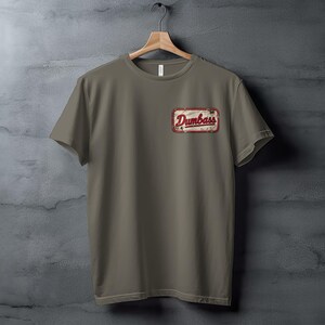 Taupe t-shirt hanging on a wooden hanger with a "Dumbass" patch.