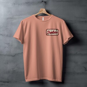 Peach t-shirt with a distressed patch reading "Dumbass" on the left chest.