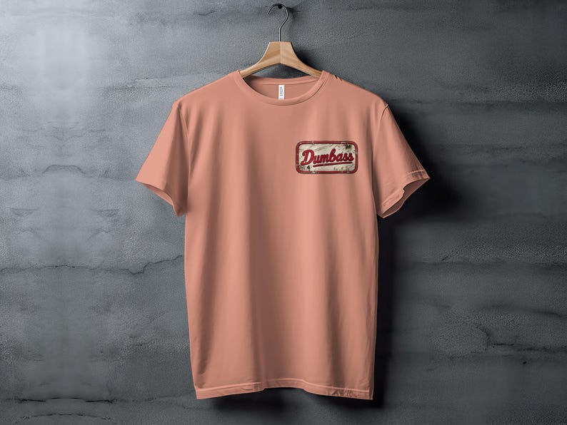 Peach t-shirt with a distressed patch reading "Dumbass" on the left chest.