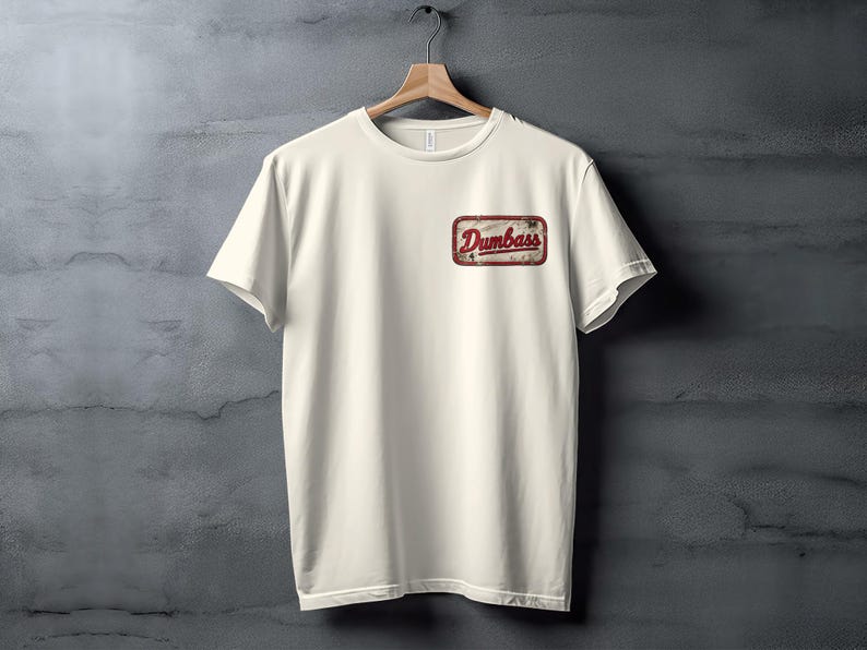 Cream t-shirt with a distressed "Dumbass" patch on the left chest.