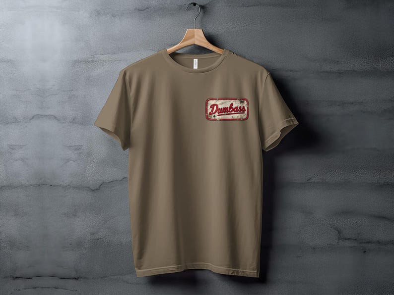 Tan t-shirt with a distressed rectangular patch reading "Dumbass" in red lettering.