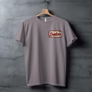 Gray t-shirt with a red and white "Dumbass" patch on the left chest.