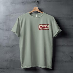 Light green t-shirt with a distressed "Dumbass" logo patch on the left chest.