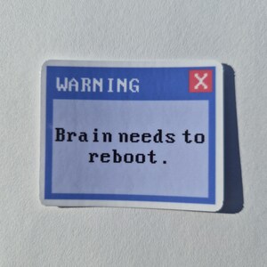 May include: A rectangular sticker featuring a blue computer warning dialog box with a white border. The text reads WARNING in the top left corner, a red square with a white X in the top right, and Brain needs to reboot. in the center.