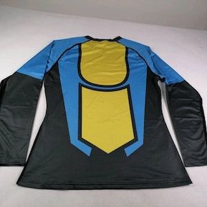 May include: A long-sleeved shirt featuring a colour-blocked design in black, bright blue, and yellow. The back displays a central yellow panel outlined in black and blue, with black sleeves and blue shoulder accents, finished with a crew neckline.
