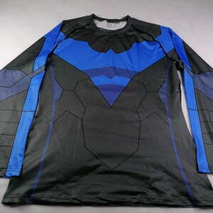 May include: A long-sleeve crew neck shirt featuring a black and blue graphic pattern. The design includes a prominent blue bird-like emblem across the chest, with black geometric paneling and blue accents extending down the sleeves and torso.