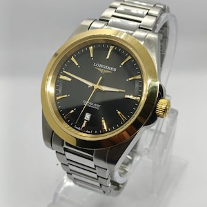 May include: A Longines Conquest Automatic wristwatch featuring a black dial with gold-tone hour markers and hands, a gold-tone bezel, and a two-tone stainless steel link bracelet. The watch includes a date window at the six o'clock position.