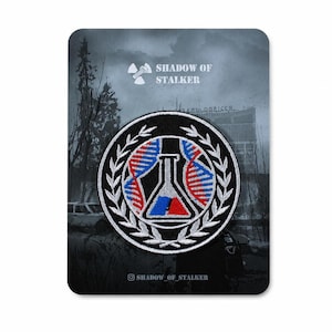 May include: A circular embroidered patch featuring a central white laboratory flask with red and blue liquid, flanked by two DNA strands in red and blue, all enclosed within a white laurel wreath on a black background, mounted on a display card.