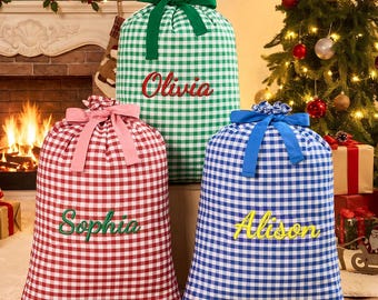 Könnte beinhalten: Drei große Geschenksäcke aus Stoff mit einem Vichy-Karo-Muster in Grün, Rot und Blau. Jeder Sack ist oben mit einer passenden Schleife zusammengebunden und mit einem Namen in Schreibschrift bestickt: Olivia in Rot, Sophia in Grün und Alison in Gelb.