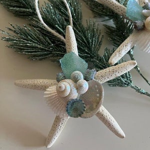 May include: White starfish Christmas ornament decorated with seashells, sea glass, and iridescent accents.
