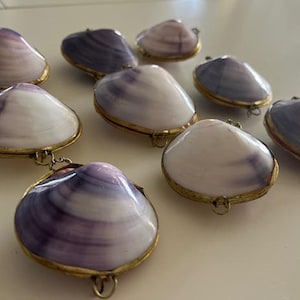 May include: A set of eight purple and white seashells with gold accents. Each shell is attached to a gold chain and has a small loop for hanging.