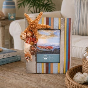May include: A decorative photo frame with a coastal theme. The frame is made of wood with colorful vertical stripes and adorned with a starfish and seashells. The frame holds a 5x7 inch photo.
