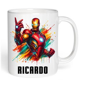 May include: A white ceramic mug featuring a colorful watercolor-style illustration of Iron Man in a red and gold suit with a glowing blue chest piece. The name RICARDO is printed in bold black capital letters at the bottom of the mug.