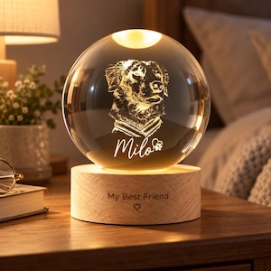 Puede incluir: Una lámpara de esfera de cristal transparente con un retrato de perro grabado con láser en su interior, el nombre Milo y un icono de huella. La esfera descansa sobre una base cilíndrica de madera clara grabada con My Best Friend y un corazón.
