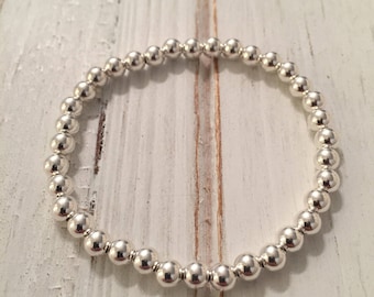 Könnte beinhalten: Ein silbernes Armband mit einem schlichten Design. Das Armband besteht aus kleinen, runden Perlen, die auf einer dünnen Schnur aufgefädelt sind.