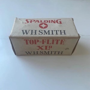 May include: A rectangular off-white cardboard box featuring the red Spalding logo and text reading WH SMITH, TOP-FLITE XL, and WH SMITH in black and red lettering. The box shows signs of wear on the edges and corners of the paper packaging.
