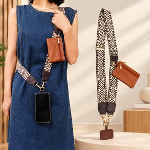 May include: A crossbody phone strap featuring a black and white geometric pattern, dark brown leather accents, and gold-tone hardware. The strap includes a detachable small brown leather zippered pouch and a clip for a smartphone.