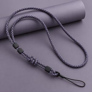 May include: A lanyard made of purple and black braided cord featuring three matte black square beads and a black metal lobster clasp. The cord is looped and knotted, ending in a thin black nylon loop for attaching small items or accessories.