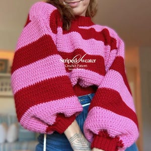Può includere: Un maglione a righe fatto a mano, in un motivo all'uncinetto. Il maglione presenta strisce orizzontali alternate rosse e rosa. Il testo "Striped Sweater Crochet Pattern" è visibile sul davanti.