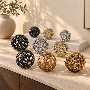 Pode incluir: Uma coleção de nove esferas decorativas em vários acabamentos, incluindo preto fosco, ouro polido e prata metálica. Cada esfera apresenta um design único de treliça vazada ou recortes circulares, criando uma aparência geométrica e texturizada.