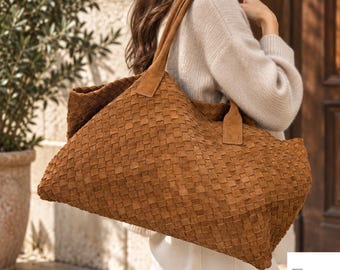 May include: A large, tan, woven suede tote bag featuring a rectangular silhouette and two sturdy shoulder straps. The exterior surface displays a consistent, intricate basket-weave pattern throughout the entire body of the bag.