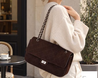 May include: A dark brown quilted shoulder bag featuring a rectangular flap, a silver-toned metal turn-lock closure, and a matching silver-toned chain strap. The bag has a textured surface with a diamond-stitched pattern throughout the exterior.