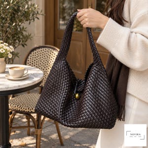 May include: A dark brown hobo bag featuring an intricate woven leather pattern, a single integrated shoulder strap, and a central gold-toned spherical button closure. The bag displays a structured yet slouchy silhouette with a consistent grid-like texture.