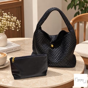 May include: A black woven hobo bag with a single braided handle and a gold-toned spherical clasp, accompanied by a matching black rectangular zippered pouch with a gold-toned zipper pull. The bag and pouch are displayed together as a set.