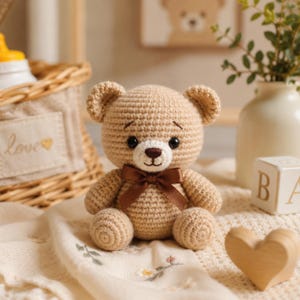 May include: A small, light brown crocheted teddy bear with a dark brown satin ribbon bow tied around its neck. The bear features black plastic eyes, a stitched dark brown nose and mouth, and a white muzzle area, crafted with a visible yarn texture.