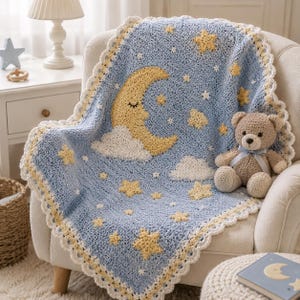 May include: A light blue crochet blanket featuring a yellow crescent moon with a sleeping face, white clouds, and yellow stars. The blanket has a white scalloped border and is draped over a chair next to a small brown teddy bear with a blue ribbon.
