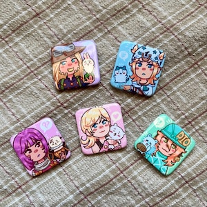 May include: Five square pinback buttons featuring colourful anime-style illustrations of characters with small creatures. The designs include a character with a hat and rabbit, a blue-themed character with a cat, a purple-haired figure, a blonde character with a heart, and a green-themed character with the text DIO.