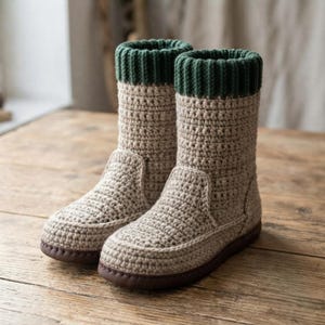 Könnte beinhalten: Ein Paar wadenhohe Stiefel mit einem beigen gehäkelten Obermaterial in strukturierter Maschenoptik und einem dunkelgrünen gerippten Strickbündchen am Schaft. Die Stiefel haben eine feste dunkelbraune Sohle und eine abgerundete Zehenpartie.