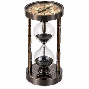 May include: An hourglass with a dark bronze metal frame and clear glass bulbs filled with black sand. The top of the frame features an integrated compass with a beige face, black markings, and a directional needle pointing towards the north.