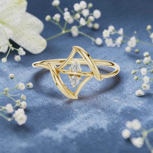 May include: A gold ring featuring a geometric, open-frame design with two small, round, clear, faceted stones set vertically in the center. The band is thin and polished, creating a delicate, angular silhouette that highlights the two sparkling stones.