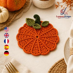 May include: A round, orange crochet coaster shaped like a pumpkin, featuring a dark green stem and three small green leaves attached to the top. The coaster has a textured, ribbed design radiating from the centre. The logo LooporaDesigns is visible.