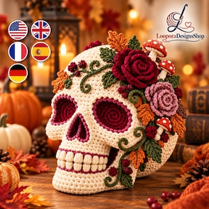 May include: A cream-colored crocheted skull decorated with dark red, pink, and orange crocheted flowers, green leaves, and small red and white spotted mushrooms. The skull features deep red eye sockets and a row of individual cream-colored teeth.